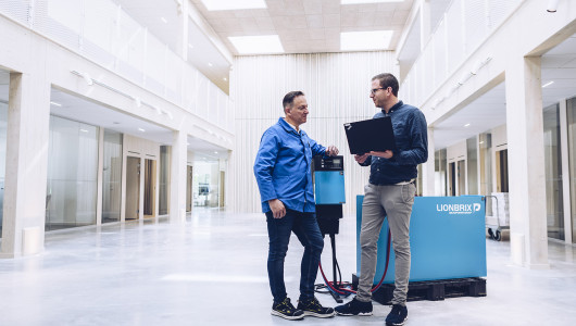 Två medarbetare står bredvid en laddare och ett batterisystem