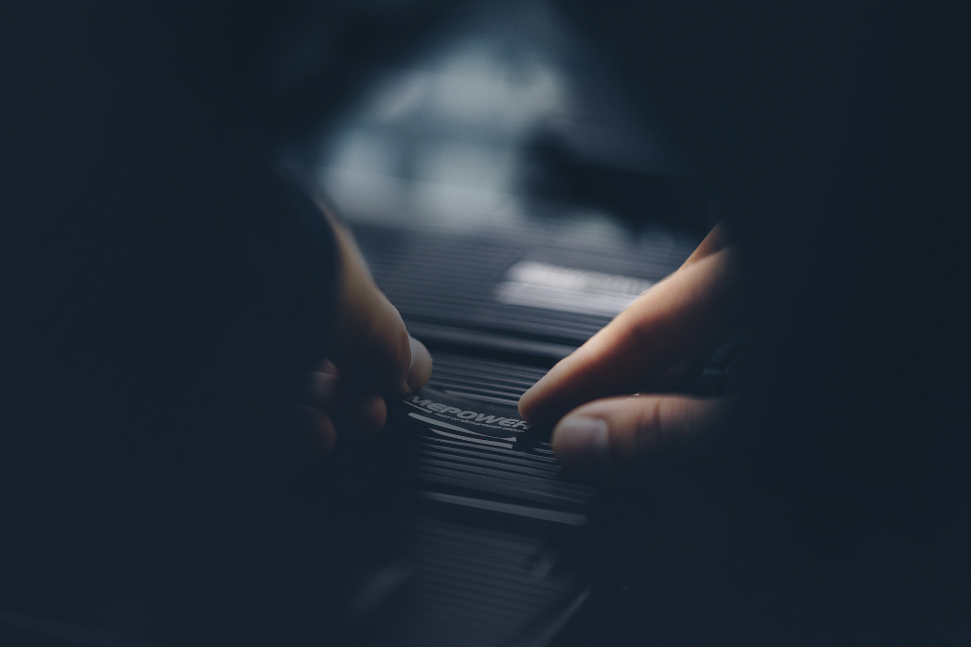 A close-up on a white mans fingers on a dcdc-converter from Micropower with a visible logotype. The light is centered in the middle of the picture with black edges.