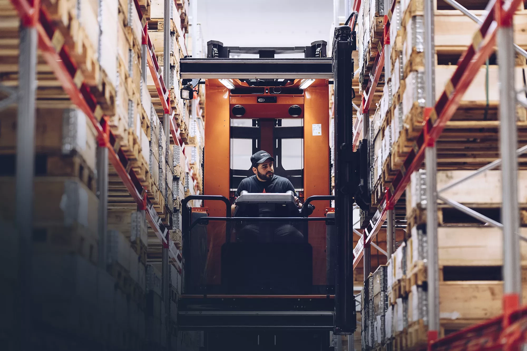 Stor orange elektrisk gaffeltruck i ett lager, styrd av en man med keps