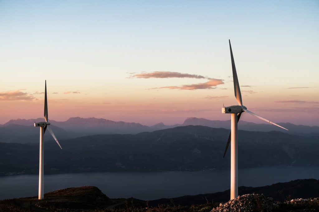 Two large wind turbines on land, at dawn or sunset.