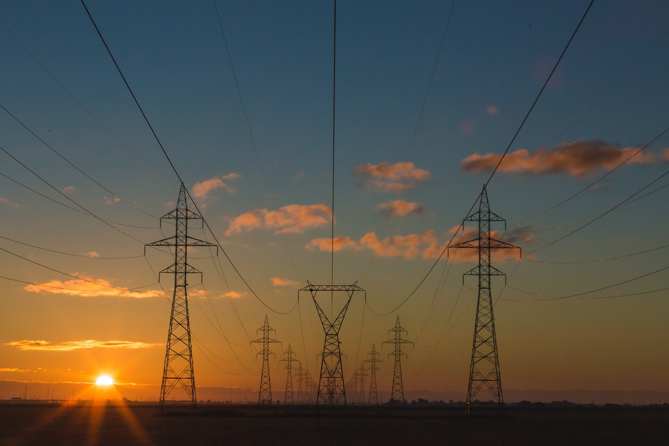 Several high voltage lines in sunset with blue sky and white clouds.