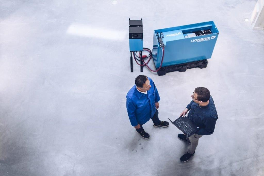 Two employees stand next to it and chargers and a battery system