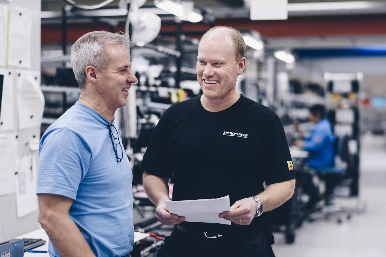 Två manliga anställda på Micropower Group pratar och ler i batterifabriken.