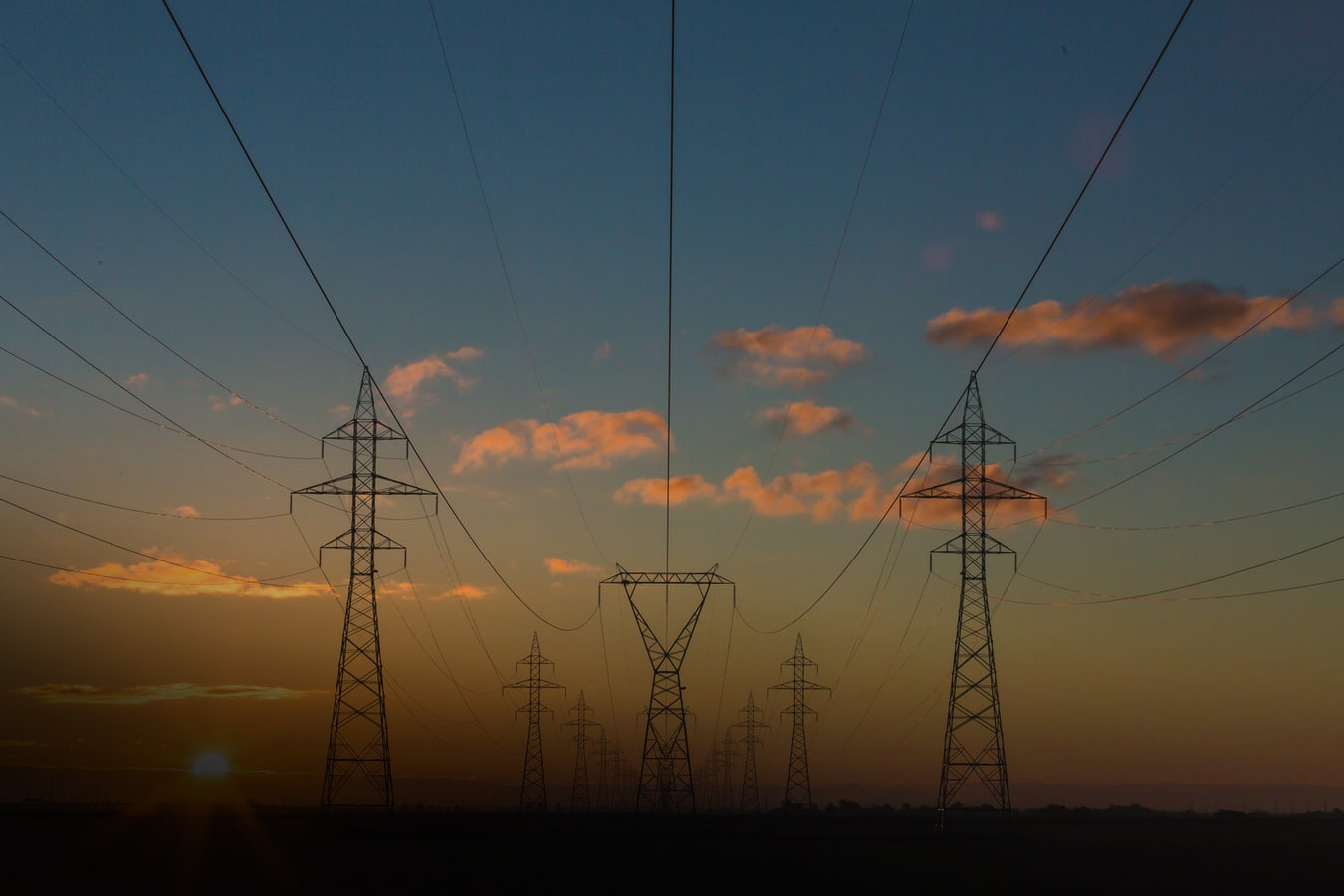 Rows of high voltage power lines at dusk/dawn with the sky in the background.